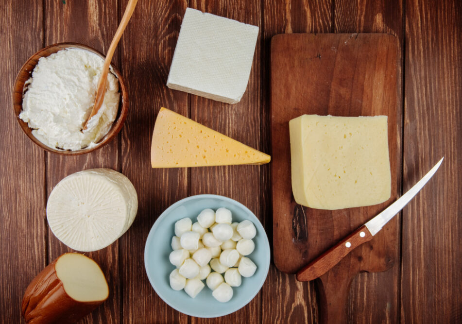 Verschiedene milde Käsesorten auf Holztisch, darunter Frischkäse, Mozzarella, Schnittkäse und Weichkäse.