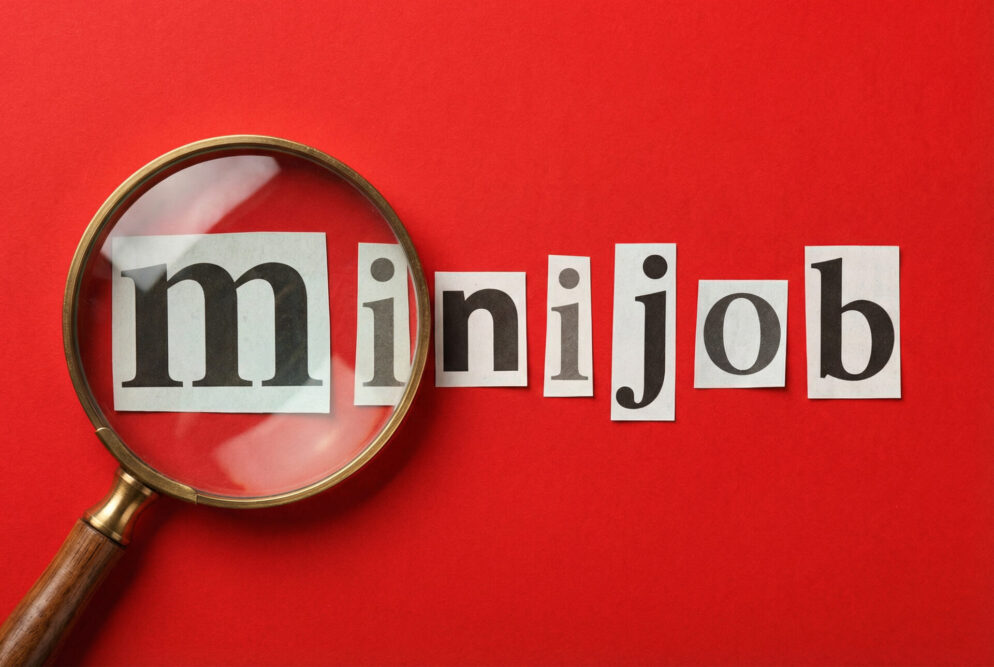 Lupe vergrößert das m im Wort minijob aus Zeitungsausschnitten auf rotem Hintergrund