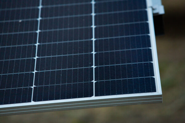Nahaufnahme eines Solarmoduls mit dunkelblauen Solarzellen und hellem Metallrahmen vor unscharfem Hintergrund.