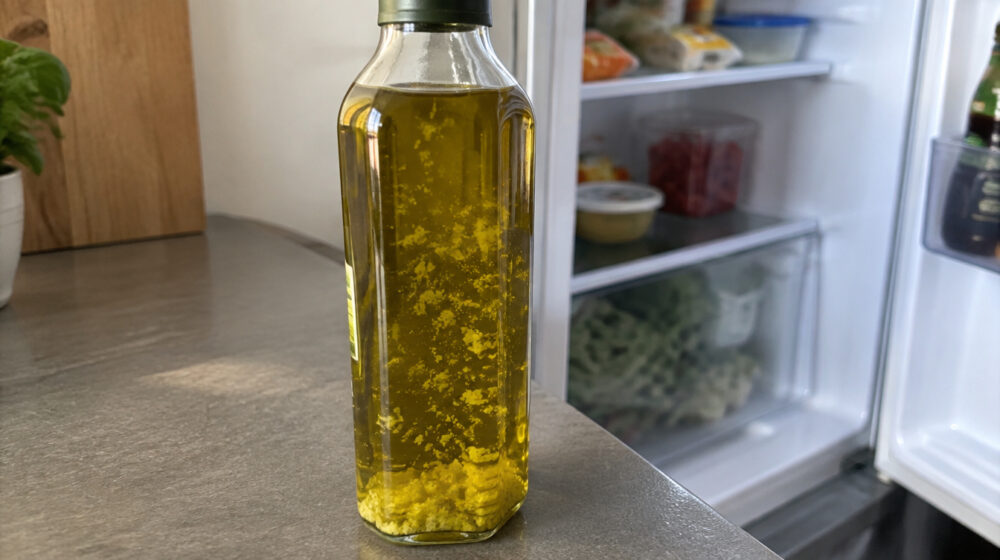 Olivenöl mit festen Flocken in einer Flasche vor geöffnetem Kühlschrank