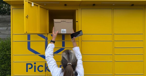 A woman using a yellow parcel locker to pick up a package in Périgueux, France.