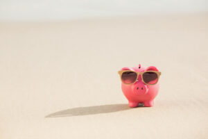 Ein entspanntes Sparschwein mit Sonnenbrille am Strand symbolisiert den Erfolg der Pay Yourself First-Methode: finanzielle Sicherheit ohne Stress.