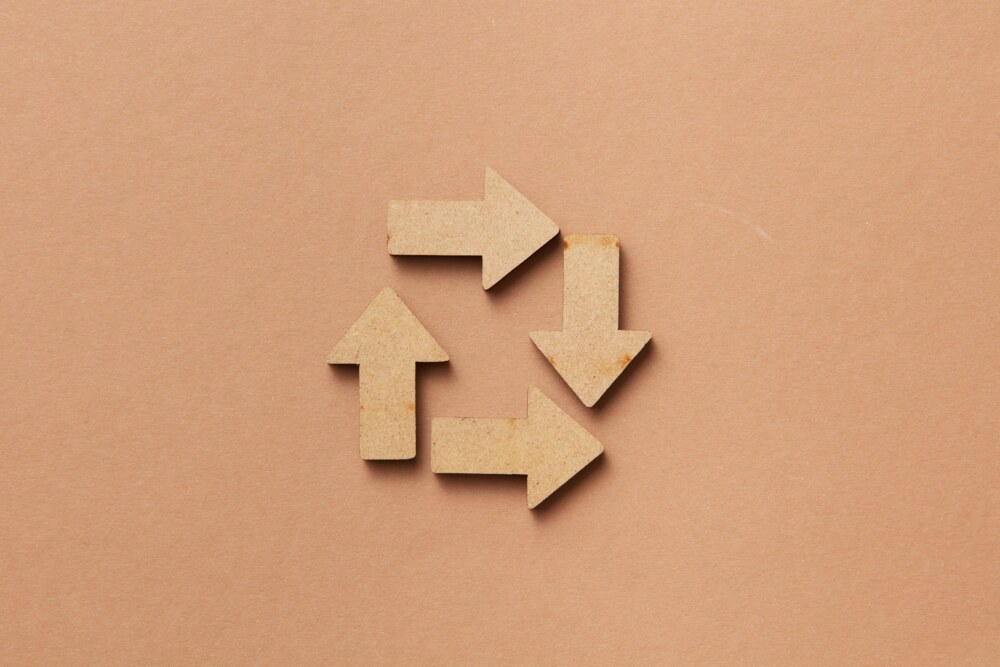Vier helle, flache Pfeile liegen auf beigem Untergrund und bilden eine kreisförmige Recycling-Symbolik.