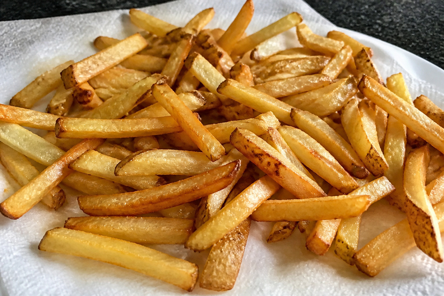 Selbstgemachte Pommes aus frischen Kartoffeln liegen goldbraun gebacken auf Küchenpapier
