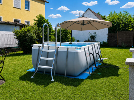 Aufstellpool im Garten mit Leiter, Sonnenschirm und Rasen als Ausgangspunkt für Pool-Verkleidungsideen