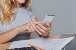 Online-Banking mit Smartphone, Rechnungen und Taschenrechner auf dem Tisch – Symbol für Dauerauftrag oder Lastschrift was ist besser bei Zahlungen.