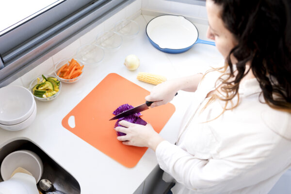 Eine Frau schneidet Rotkohl mit einem Messer auf einem orangefarbenen Schneidebrett in der Küche.