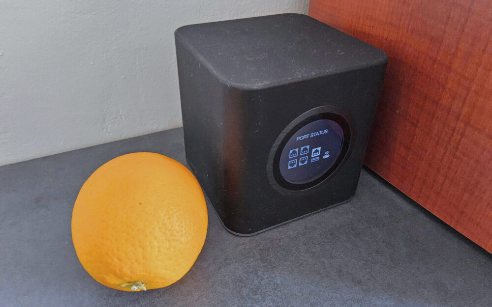 in schwarzer Router mit matter, klebriger Soft-Touch-Oberfläche steht auf einem Regal neben einer Orange - Beispielbild für die Reinigung solcher Geräte.