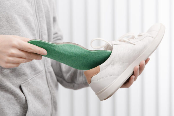 Person entfernt grüne Einlegesohle aus weißem Sneaker, um Schuhe geruchsfrei zu halten