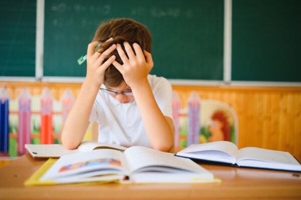 Junge sitzt mit Schulfrust über Schulbüchern im Klassenzimmer