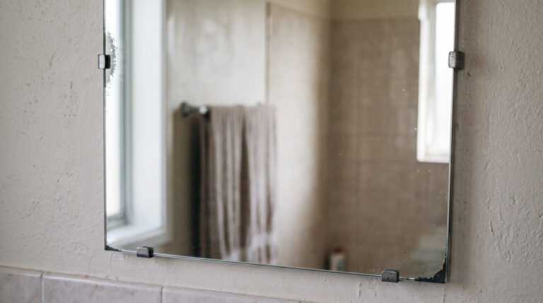 Badezimmerspiegel mit schwarzen und grauen Flecken an den Rändern durch eine beschädigte Spiegelschicht.