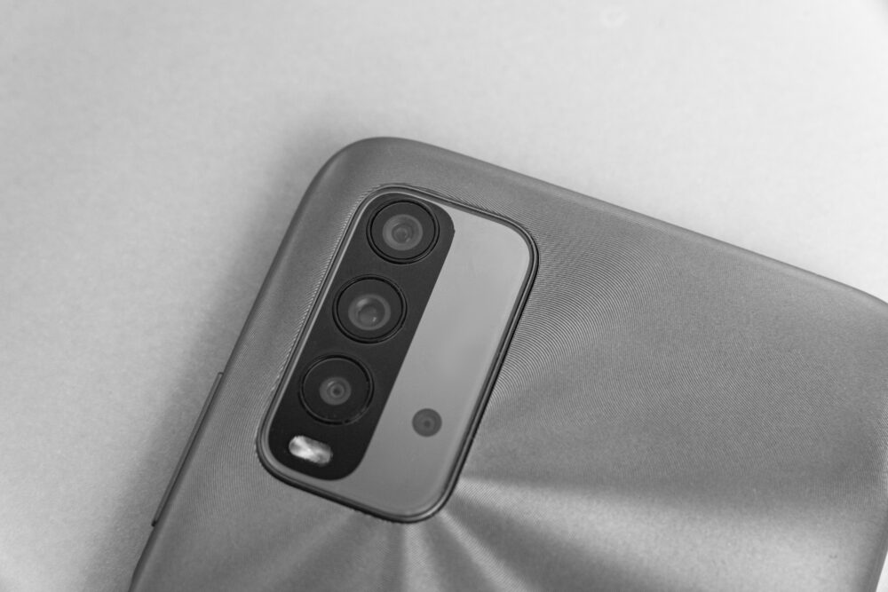 Nahaufnahme der Rückseite eines Smartphones mit drei übereinander angeordneten Kameralinsen und einem Blitz.