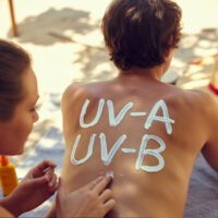 Sonnencreme-Schriftzüge „UV-A“ und „UV-B“ auf dem Rücken eines Mannes am Strand