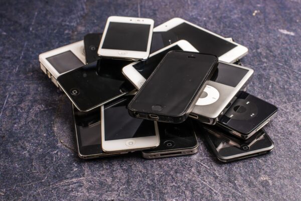 Mehrere ältere Smartphones und tragbare Musikplayer liegen übereinandergestapelt auf einer dunklen, rauen Oberfläche.
