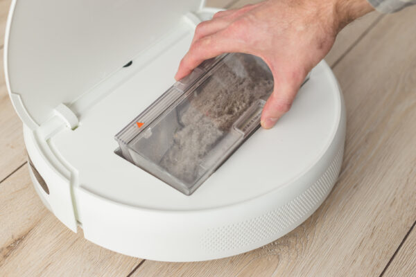 Eine Hand zieht den transparenten, mit Staub und Schmutz gefüllten Behälter aus einem weißen Saugroboter.