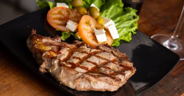 Delicious grilled steak served with fresh salad and feta cheese on a black plate.