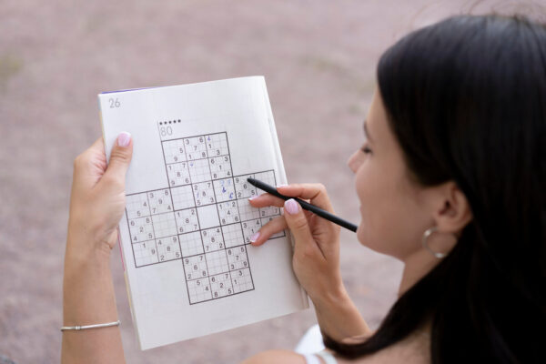 Frau löst ein komplexes Sudoku in einem Rätselheft mit Bleistift.