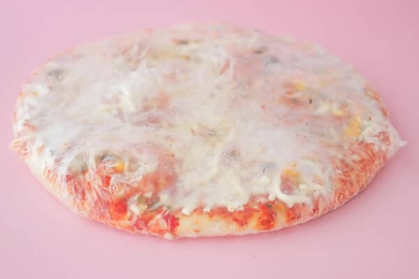 Eine tiefgekühlte Pizza in transparenter Verpackung auf rosafarbenem Hintergrund