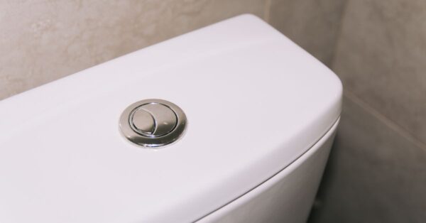 Close-up of a modern dual flush toilet with a chrome button, highlighting clean and contemporary design.