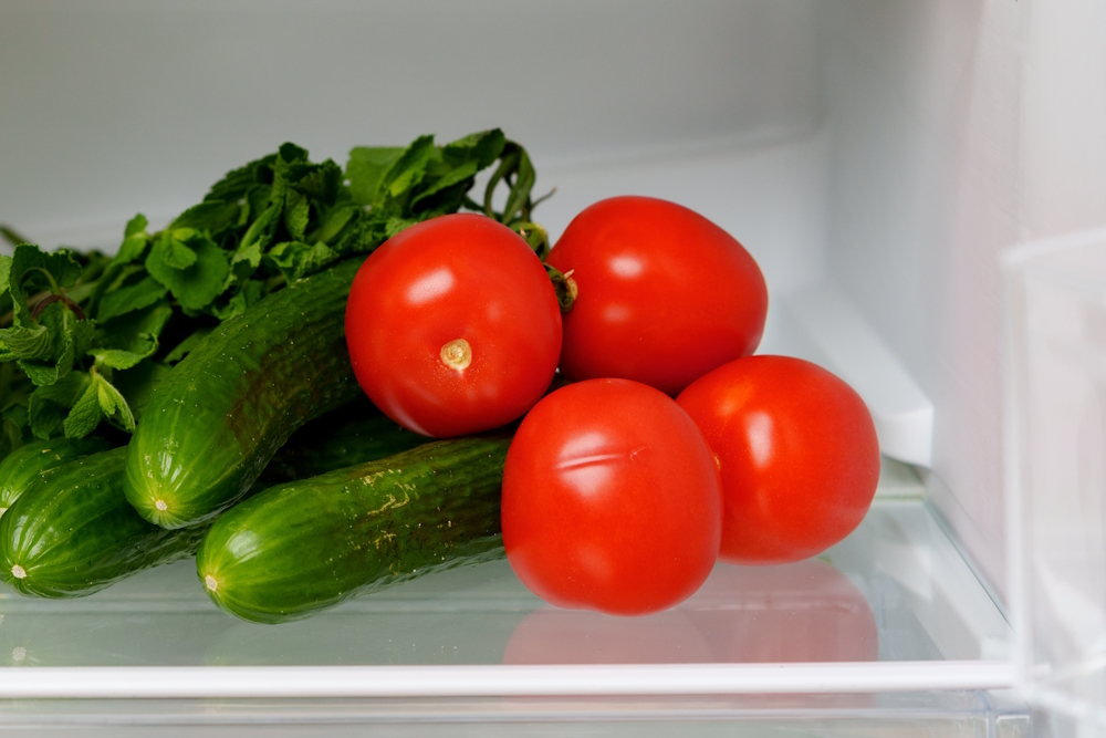 Tomaten liegen neben Gurken im Kühlschrank