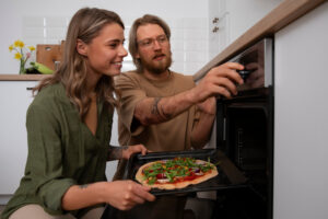 Zwei Personen schieben gemeinsam eine belegte Pizza in den Backofen