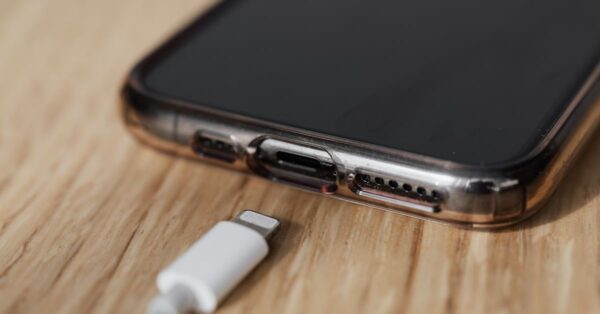 Modern cellphone in transparent cover with closeup of charging input and mobile phone white charger cable usb connector on wooden table
