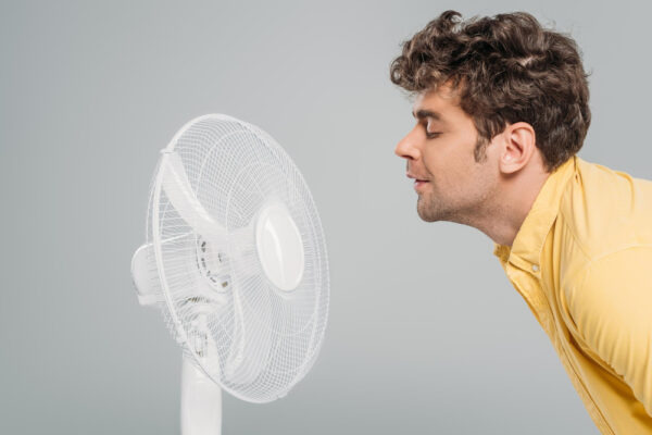 Mann beugt sich vor einen Ventilator, um sich an einem heißen Tag abzukühlen