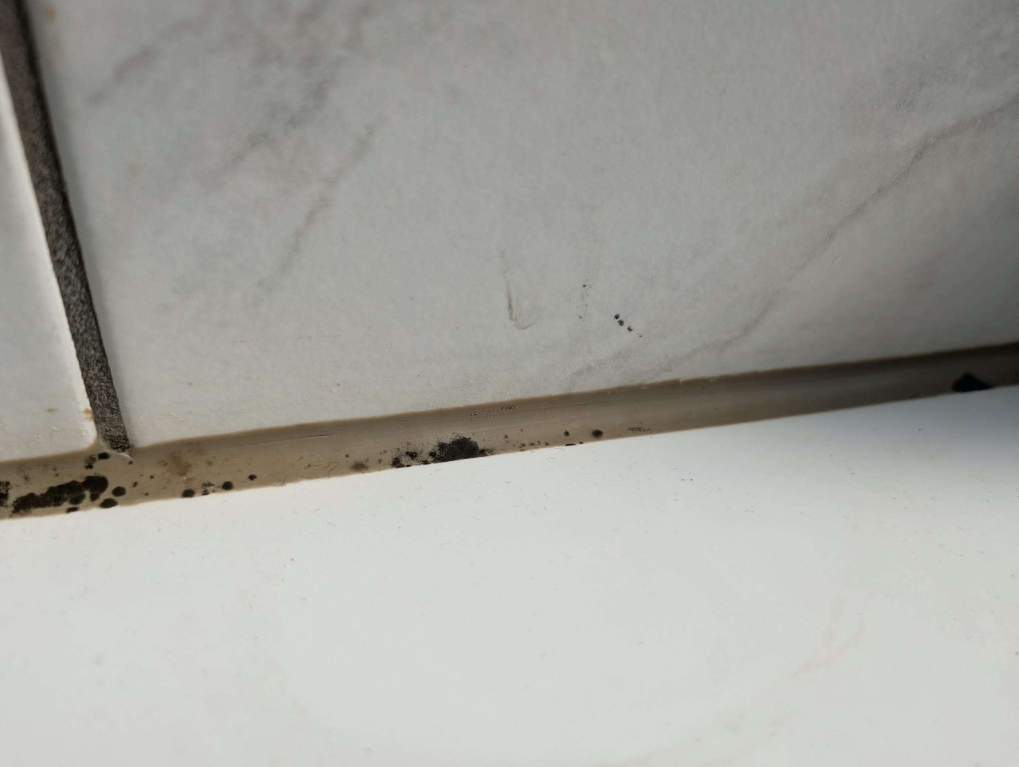 Verfärbte Silikonfuge im Bad mit schwarzen Flecken und dunklen Ablagerungen