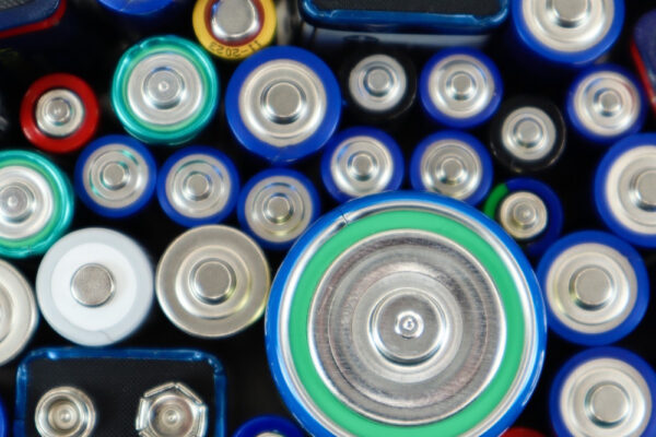 Draufsicht auf eine dichte Ansammlung verschiedener Batterien, die eng nebeneinander liegen. Zu sehen sind unterschiedliche Größen wie AA, AAA und ein 9V-Block sowie diverse Farben (Blau, Silber, Grün), was an eine typische Sammelbox für Batterien erinnert.