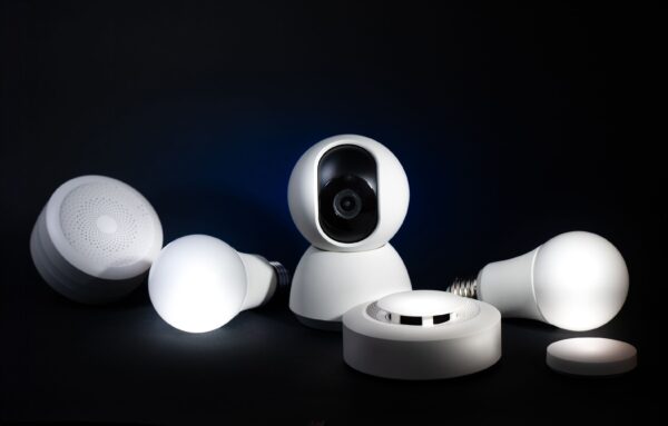 Mehrere weiße Smart-Home-Geräte stehen vor dunklem Hintergrund, darunter eine Kamera, runde Sensoren und zwei Lampen.