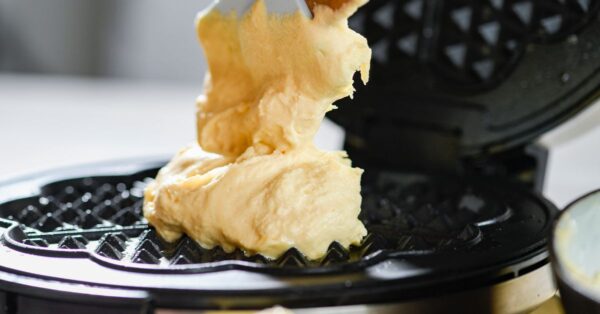 Delicious waffle batter being spread on a waffle maker for a tasty breakfast.