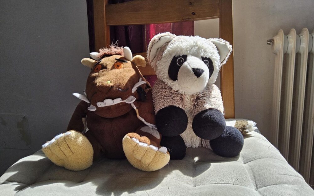 Zwei Warmies, Grüffelo und Waschbär, sitzen nebeneinander auf einem Stuhl und warten auf ihren Einsatz als Wärmekissen.