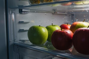 Rote und grüne Äpfel liegen in der Gemüseschublade im Kühlschrank, in dem sich Wasser gebildet hat.