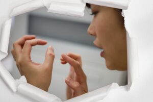 Frau betrachtet kleinen Schnitt am Finger, gerahmt von gerissenem Papier