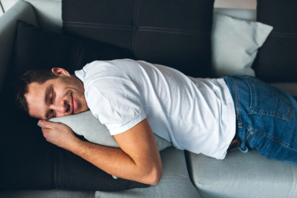 Was ist Powernapping: Mann macht einen kurzen Powernap auf dem Sofa und schläft mit dem Kopf auf einem Kissen.