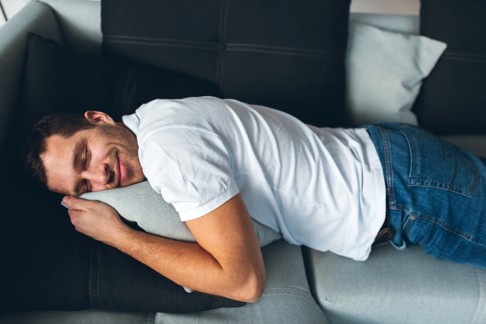 Was ist Powernapping: Mann macht einen kurzen Powernap auf dem Sofa und schläft mit dem Kopf auf einem Kissen.