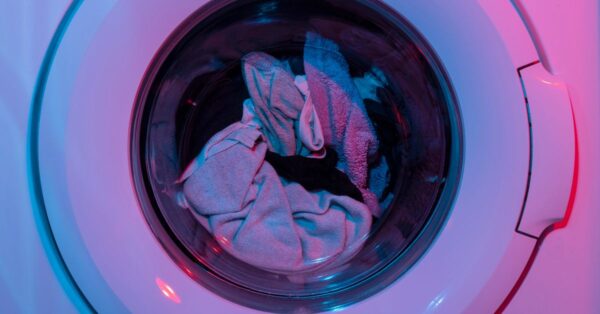 Colorful washing machine with clothes inside, lit by vivid purple and blue lights.
