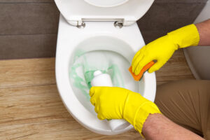 Person mit gelben Gummihandschuhen reinigt die Toilettenschüssel mit selbstgemachtem WC-Reiniger und Schwamm.