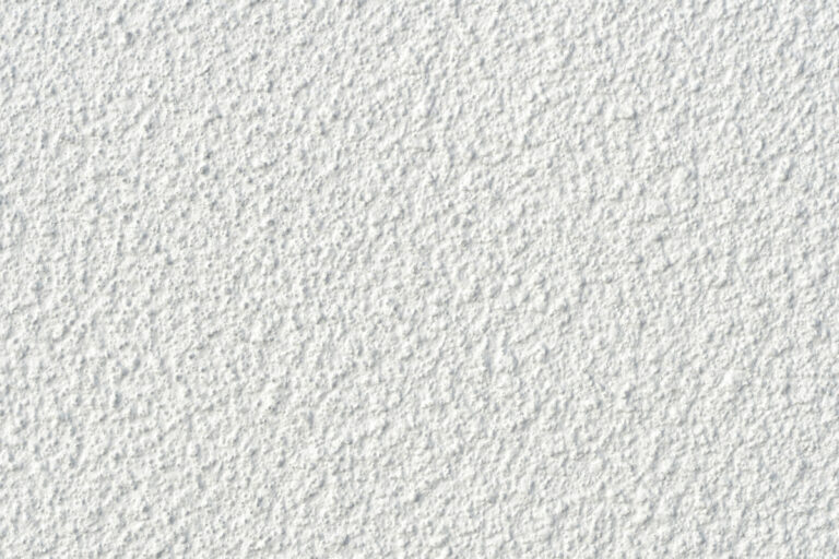 Nahaufnahme einer weißen Wand mit grober, unregelmäßiger Struktur und vielen kleinen Erhebungen und Vertiefungen.