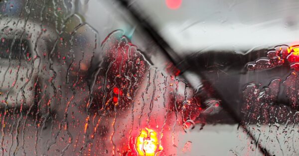 Raindrops on a car windshield with blurred traffic lights on rainy day.