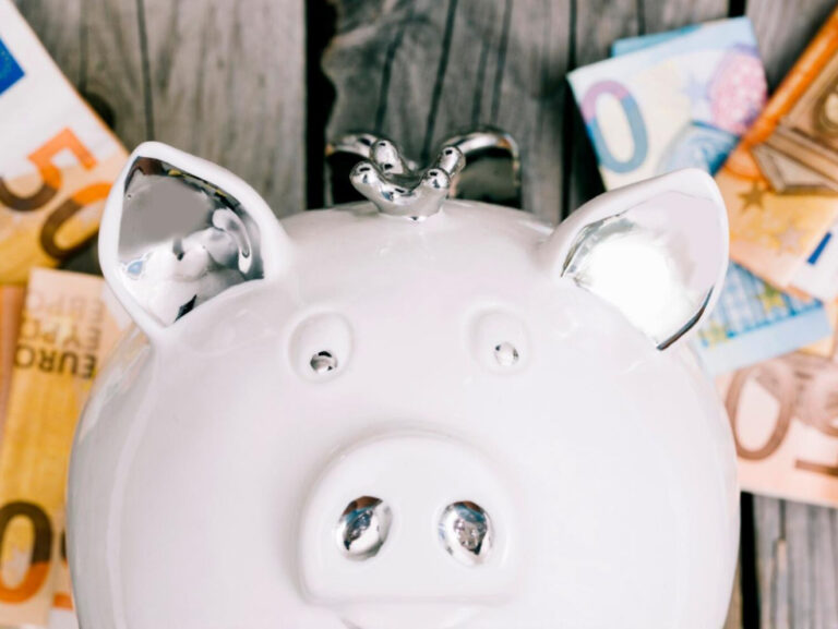 Weißes Sparschwein mit Eurobanknoten als Symbol dafür, wie hoch der Notgroschen sein sollte