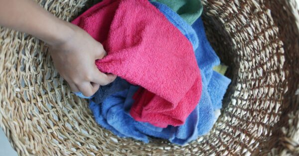 Hand greift in einen Wäschekorb mit bunten Handtüchern