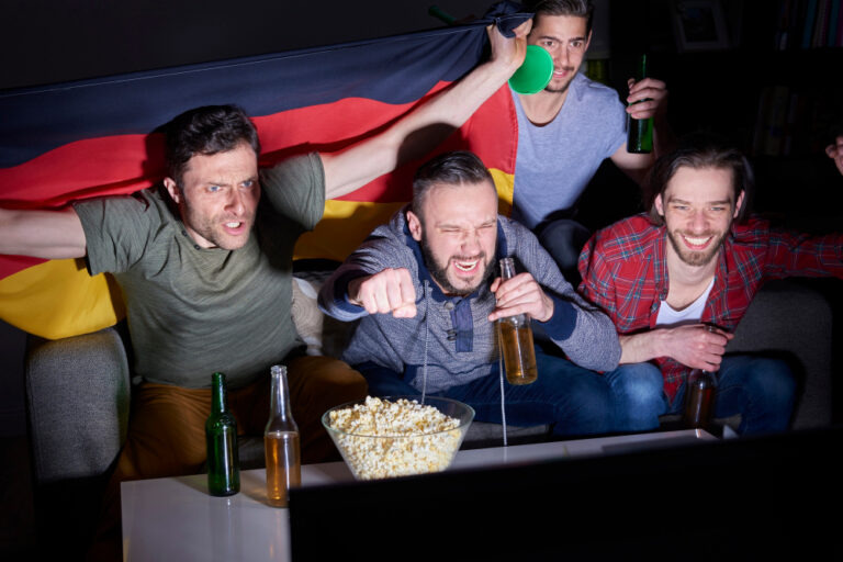 Freunde schauen ein Fußballspiel mit Deutschlandflagge im Wohnzimmer
