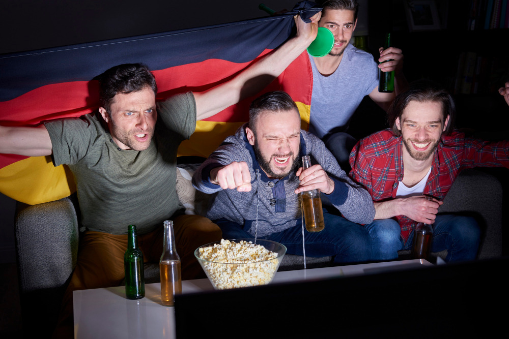Freunde schauen ein Fußballspiel mit Deutschlandflagge im Wohnzimmer