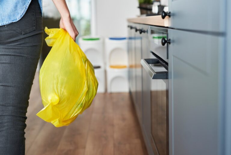 Frau trägt gefüllten gelben Sack aus der Küche als Symbolbild für den Ratgeber: Was kommt in den gelben Sack?