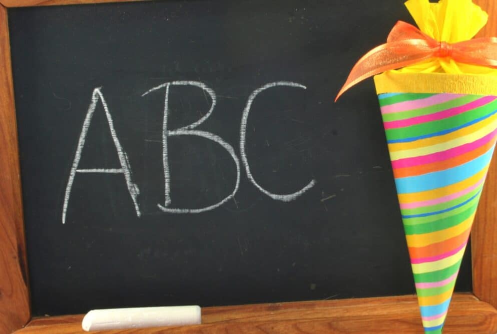 Kleine Tafel auf der mit Kreide geschrieben ABC steht, am rechten Rand eine Schultüte als Symbolbild für den Ratgeber: Was schenkt man zur Einschulung?