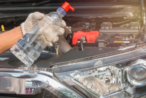 Selber gemachtes destilliertes Wasser wird von einer Person vor geöffneter Motorhaube gehalten