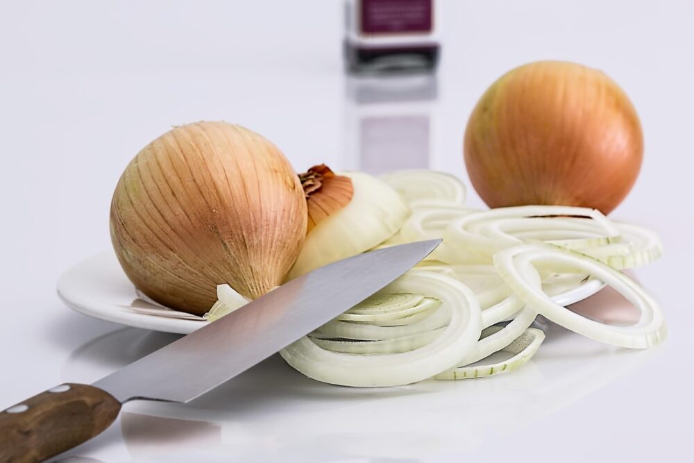 Ganze und in Ringe geschnittene Zwiebeln neben einem Küchenmesser